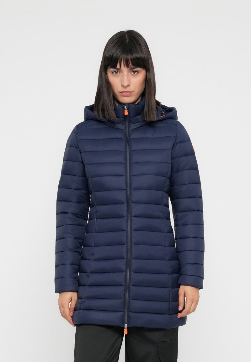 Navy pufferjack met horizontale stiksels, ritssluiting aan de voorkant en een verstelbare capuchon. Kenmerkend zijn de oranje accenten en het slanke, verlengde ontwerp.