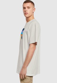Lys grå bomulds t-shirt med et flerfarvet geometrisk grafisk design på forsiden, med en løs pasform og korte ærmer.