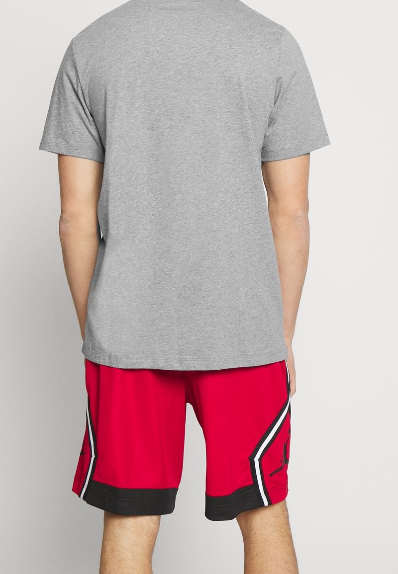 Personne portant un t-shirt gris à manches courtes et un short de basketball rouge avec des bandes latérales noires et blanches, de dos.
