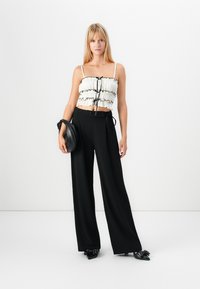 Top corto bianco con bordo a volant nero e legatura frontale, abbinato a pantaloni neri a vita alta e gamba larga e scarpe nere con punta a punta.