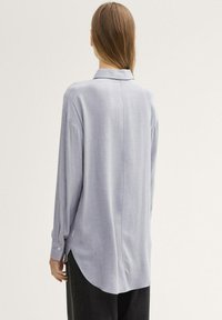 Camicia a maniche lunghe blu chiaro con vestibilità relax, orlo curvo e polsini abbottonati. Tessuto liscio con una sottile lucentezza. Vista posteriore.