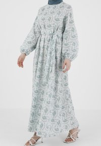 Pitkähihainen vaaleansininen mekko kukkakuviolla, vyötäröltä kireä ja virtaava siluetti. Yhdistetty valkoisiin nauhakorkokenkiin.