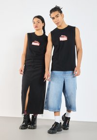 Mustad käised t-särgid, millel on punane Marvel logo, koos musta denim seelikuga, millel on lõhik, ning helesiniste laia säärega teksadega. Mustad saapad ja spordijalatsid.