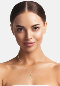 Goldene Kette mit einem Anhänger in Form eines Violinschlüssels. Feine Glieder und glatte Textur. Das Model hat einen gleichmäßigen Hautton mit dezentem Make-up.