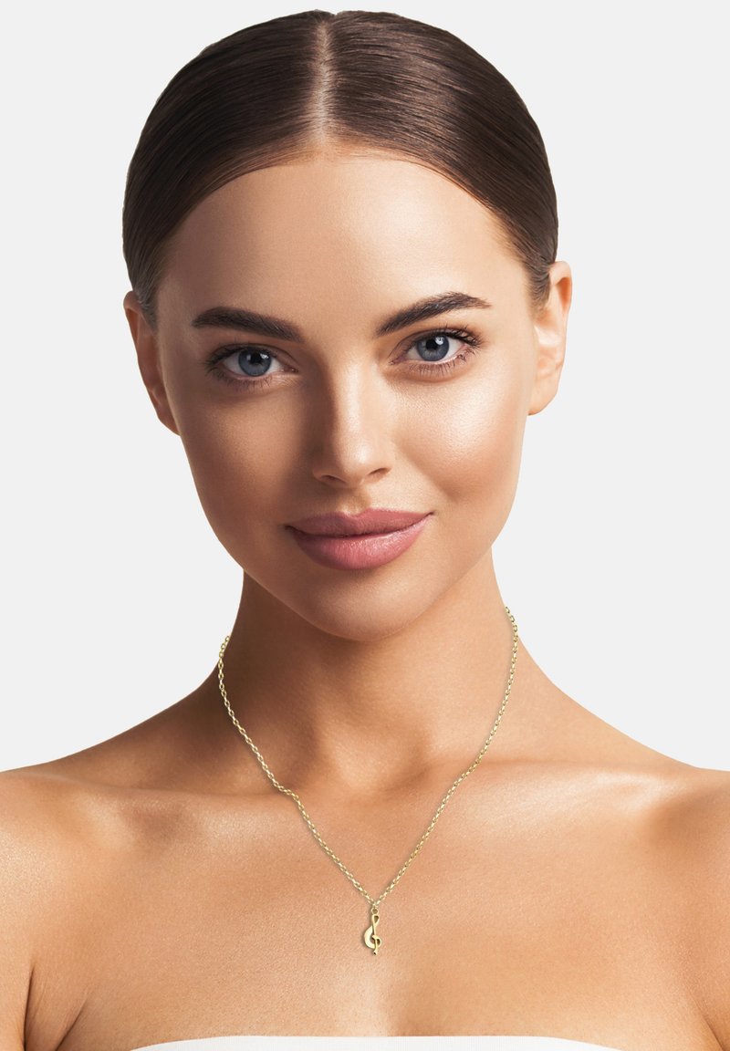 Goldene Kette mit einem Anhänger in Form eines Violinschlüssels. Feine Glieder und glatte Textur. Das Model hat einen gleichmäßigen Hautton mit dezentem Make-up.