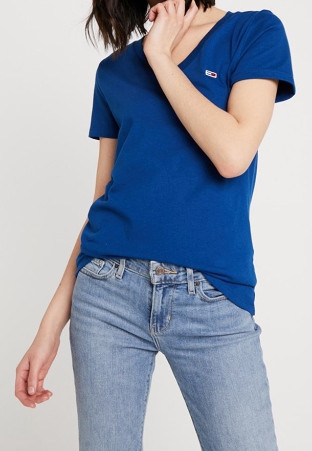Royal blue cotton T-shirt with a v-neck, short sleeves, and a small logo patch on the left chest; paired with light blue jeans.