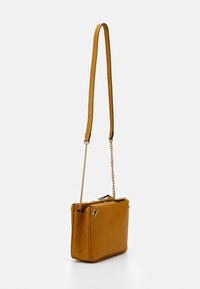 Borsa color giallo senape con superficie testurizzata, dotata di tracolla a catena e chiusure con doppia cerniera. Forma compatta e rettangolare.