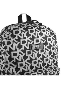 Mochila DKNY en blanco y negro con un llamativo patrón de logo, material de tela, cierre de cremallera y un asa superior para llevar.