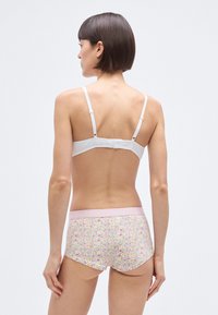 Balta liemenėlė su reguliuojamomis petnešėlėmis ir aukštu liemeniu pasiūtas apatinis trikotažas su gėlių raštu, minkštu rožiniu liemeniu. Lygi tekstūra, funkcionalus dizainas.