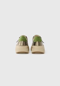 Un paio di sneaker spesse con suole beige, corpo in oro metallico e colli del tallone in suede verde, viste da dietro su uno sfondo bianco.