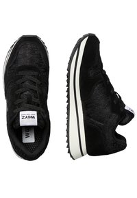 Sneakers atletici neri con una tomaia in tessuto testurizzato, chiusura con lacci, logo bianco inserito e suola in gomma con una leggera striscia nera e bianca.