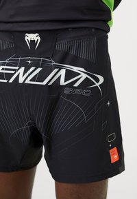 Schwarze Sportshorts mit einem eleganten Design und blauen grafischen Mustern. Enthält ein Logo und ein kleines rotes Etikett mit Markendetails.