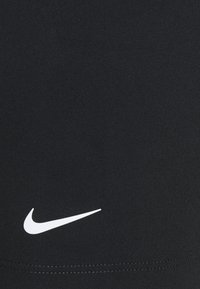 Sorte athletiske leggings laget av glatt, elastisk stoff med en hvit Nike swoosh-logo på nedre del av benet. Har rene sømmer og ingen mønstre.