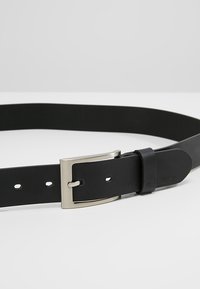 Sort læderbælte med en sølvmetalspænde, der har huller til justering og en glat overflade. Simpelt, minimalistisk design.