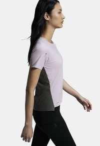 Light pink athletic t-shirt with short sleeves and a grey side panel. Smooth fabric with subtle texture. Worn with black leggings.