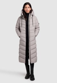 Manteau long matelassé avec un col haut et une capuche. Tissu gris clair avec un motif en chevrons, doté de poches latérales et d'une fermeture éclair. Accents noirs.