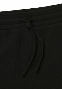 Joggers noirs en tissu texturé avec une taille élastique et un cordon de serrage, présentant une poche latérale et un fit confortable.