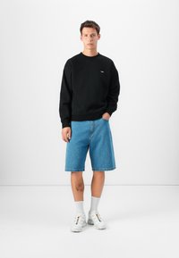 Črna majica s kratkimi rokavi z okroglim izrezom, kombinirana s svetlo modrimi denim šortsi. Bele superge in bele nogavice dopolnjujejo obleko.