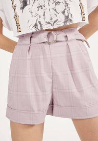 Lyse lilla rutete shorts med belte i midjen, prydet med en sølvring og pent rullet kant; mykt stoff med en glatt tekstur og subtil glans.