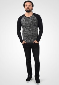 Svart langermet T-skjorte med en strukturert grå kropp og ensfargede svarte ermer, parret med svarte jeans og svarte joggesko.