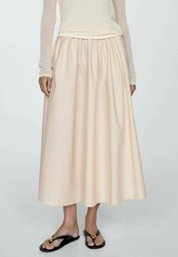 Falda midi de melocotón pálido con cintura fruncida, hecha de un tejido ligero, que presenta un diseño fluido y se combina con sandalias planas negras.