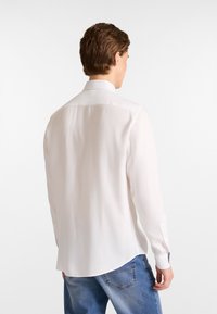 Witte lange mouwen shirt met een standaard kraag, gladde textuur en knoopmanchetten, gecombineerd met blauwe spijkerbroek.