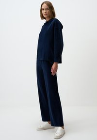 Haut à capuche en velours bleu marine et pantalon assorti, avec une coupe décontractée, des manches longues et une texture subtile, associés à des baskets blanches.