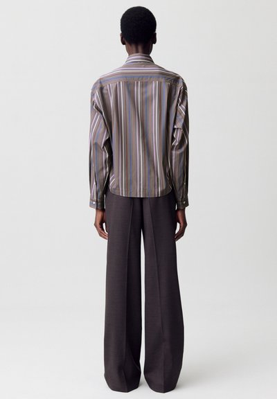 Camicia a righe con maniche lunghe nelle tonalità di marrone, blu e viola, abbinata a pantaloni grigi a gamba larga. Texture liscia e dettagli con bottoni.
