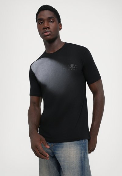 Svart T-shirt med kort ärm, featuring ett gradient grått mönster med en tryckt design nära axeln. Matchat med ljusblå jeans.