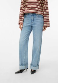 Vaqueros de mezclilla azul claro con un ajuste relajado, dobladillos remangados y detalles de costura sutiles, combinados con un top a rayas burdeos y crema.