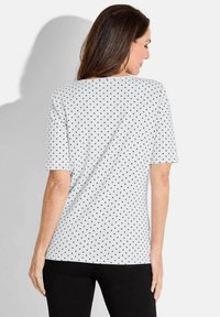 Witte T-shirt met zwarte stippen, korte mouwen, een ontspannen pasvorm en een ronde hals. De stof lijkt zacht en textuur te hebben.