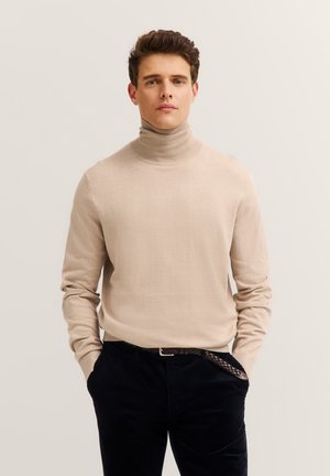 Beige Rollkragenpullover mit langen Ärmeln, weicher Textur, taillierte Passform, kombiniert mit dunkelbraunen Cordhosen und einem geflochtenen Leder-Gürtel.