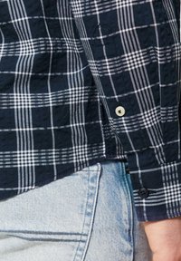 Donkerblauwe geruite shirt met witte lijnen, voorzien van knoopmanchetten en een getextureerde stof. Gemaakt boven lichtblauwe spijkerbroek.