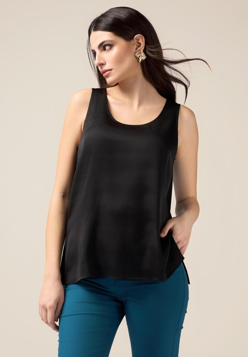 Top in satin nero con scollatura a barca e spacchi laterali, abbinato a pantaloni fitted color teal. Texture liscia con una leggera lucentezza.