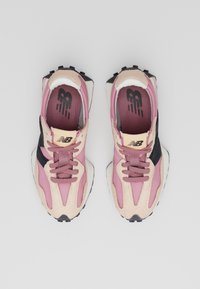 Pár růžových a béžových tenisek New Balance s černými akcenty, pohled shora, na jednoduchém světlém šedém pozadí.