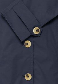 Marineblaues Hemd mit glatter Textur, strukturiertem Kragen und großen, runden goldenen Knöpfen mit schwarzer Naht.