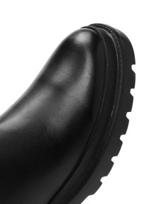 Bota de cuero negro hasta el tobillo con puntera redondeada, parte superior texturizada y suela de goma gruesa con profundas ranuras para mejorar la tracción.