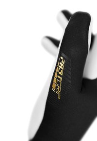Guante negro con una superficie texturizada y puntas blancas. Presenta un logo dorado en la zona de la muñeca, destacando su diseño.