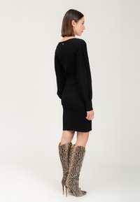 Zwarte geribbelde gebreide jurk met lange mouwen en een sleutelgatdetail op de rug, gecombineerd met kniehoge slangenprint stiletto laarzen.