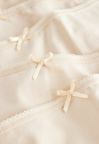 Soft beige fabric with delicate lace trim and small satin bows arranged in overlapping rows.