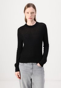 Svart ribbstrikket genser med rund hals, lange ermer og tettsittende kant. Bæres med lysegrå, løstsittende jeans.