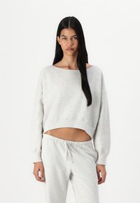 Sweatshirt gris raccourci avec un col large et des manches longues, associé à un pantalon de survêtement gris assorti avec une taille élastique.