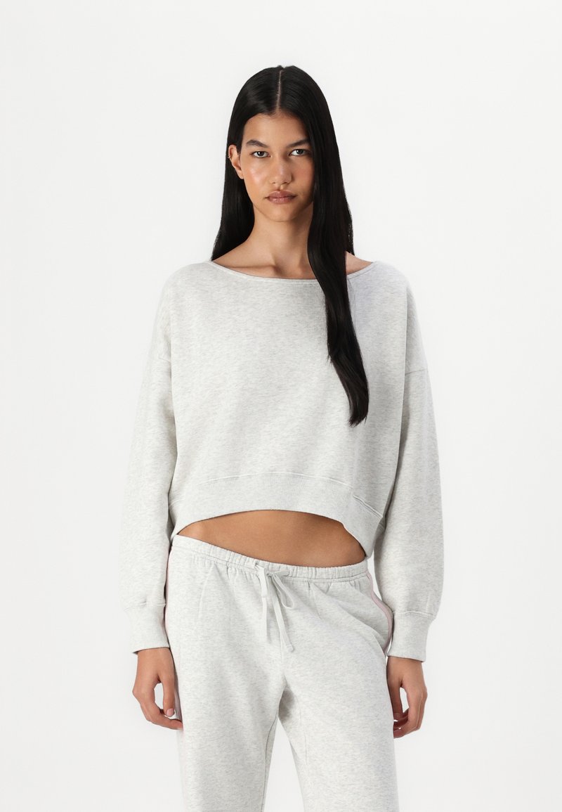 Felpa grigia corta con scollo ampio e maniche lunghe, abbinata a pantaloni tuta grigi coordinati con cintura elasticizzata.