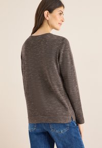 Maglione marrone a maniche lunghe con una texture sottile, spacchi laterali e una vestibilità rilassata, abbinato a jeans blu.