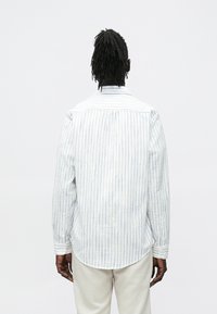 Koszula z długim rękawem w pionowy, jasnoniebiesko-biały pasek, z mankietami na guziki i zaokrąglonym dołem. Wykonana z lekkiego materiału.