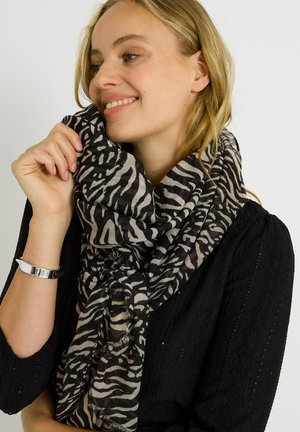 Bufanda con estampado de cebra en negro y gris, hecha de tela ligera, con extremos con flecos, llevada de manera suelta alrededor del cuello sobre una blusa negra.