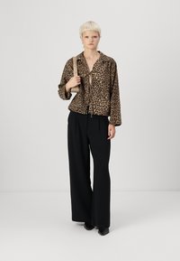 Leopard print jack met een strik voor, lange mouwen en een zwarte, hoge taille, wijde broek. Soepele textuur, neutraal kleurenpalet.
