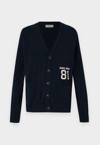 Tamsiai mėlynas kardiganas su V formos iškirpte, su skylėm rankovėse ir apačioje, turi dvi priekines kišenes ir "GUESS JEANS" logotipą su numeriu 81 kairėje pusėje.