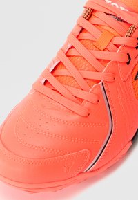 Pantof sportiv neon portocalie cu un upper texturat, sireturi proeminente și un design elegant. Prezintă un logo și detalii de cusătură subtile.