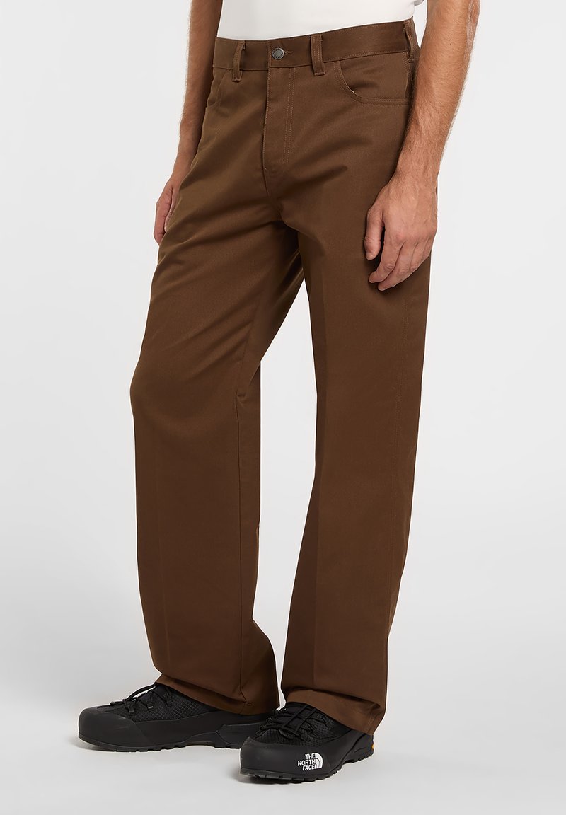 Brown, straight-leg pants made of sturdy fabric, featuring a button closure and standard pockets, paired with black hiking shoes.